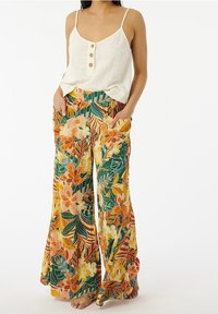 Débardeur en lin léger avec trois boutons en bois, associé à un pantalon ample à motif floral dans des couleurs vibrantes d'orange, de vert et de jaune.