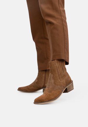 Hnědé semišové kotníkové boty s texturovaným vzorem hadí kůže, vroubkovaným designem s vlnitými okraji a žebrovanými detaily na svrchní části, s vrstveným podpatkem.