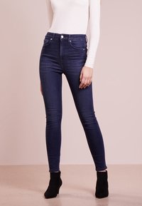 Vaqueros ajustados en denim de lavado oscuro con sutiles bolsillos frontales, cintura alta y una textura suave. Combinados con botines negros.