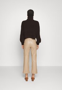 Pull col roulé marron côtelé associé à un pantalon en cuir beige taille haute, avec jambes droites et poches arrière. Sandales marron à talons.