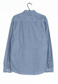 Košile s dlouhým rukávem z jemného modrého chambray materiálu, s límečkem na knoflíky, zadním yoke a manžetami s knoflíky. Hladká textura.