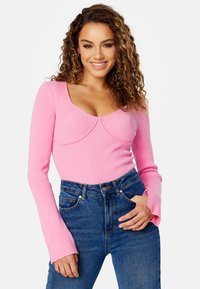 Maglietta lunga a righe rosa con scollo a barchetta e dettagli cuciti. Abbinata a jeans in denim blu a vita alta.