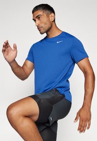 Sinine Nike sportlik t-särk lühikeste varrukatega, niiskust eemal hoidvast kangast, koos mustade lõhikutega lühikestega, millel on tekstuurilised aktsendid.
