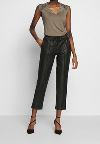 Olive green sleeveless top with lace detailing at shoulders, paired with black faux leather tapered pants and strappy black heels.
