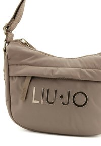 Borsa a spalla in nylon beige con chiusura a zip, dotata di una tracolla testurizzata e dettagli metallici con il logo. Superficie liscia con una leggera lucentezza.