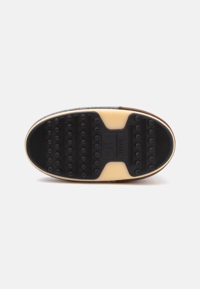 Semelle de chaussure avec une bande de roulement en caoutchouc noir comportant des crampons ronds et des rainures sur une base beige clair, conçue pour la traction et la durabilité.