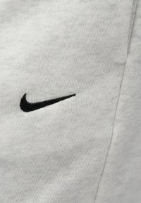 Φόρμες Nike σε ανοιχτό γκρι ύφασμα, με μαύρο κεντημένο λογότυπο swoosh. Ομαλή  υφή με διακριτικό πρότυπο ύφανσης.
