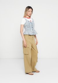 Licht denim peplumtop met knoopsluiting, laag over een wit T-shirt met rode halslijn; gecombineerd met kaki cargobroek met zijzakken.