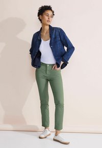 Tummansiniset farkkutakki, valkoinen toppi, vihreät mittatilauspanssarit ja valkoiset lenkkitossut, joissa on vaaleanruskea pohja. Sileä kangas ja istuva muotoilu.