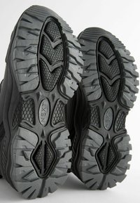 Zwarte sportieve schoenzolen met een robuust profiel, voorzien van een gestructureerd rubber en diepe groeven voor grip en stabiliteit.