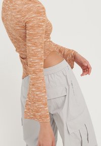 Oranžový žebrovaný top s dlouhým rukávem a rozšířenými manžetami, kombinovaný se světle šedými cargo kalhotami s bočními kapsami a elastickým pasem.