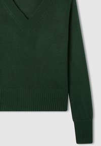 Ciemnozielony sweter robiony na drutach z dekoltem w kształcie V. Posiada prążkowane mankiety i dół, z gładką teksturą na całej powierzchni. Idealny do warstwowego noszenia.