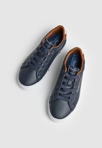 Tumes nahkased tennisetossud pruunide aktsentidega, valge kummist tallaga, ümar nina ja lukkudega disain, mis sisaldab tekstuuriga kangast ja logo detaile.