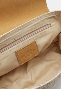 Interior de bolsa de tela beige con un pequeño bolsillo con cremallera y una etiqueta de cuero cosida dentro del forro.