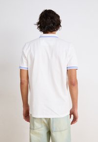 Hvid polo shirt med blåt stribet ribkant ved kraven og ærmekanterne. Blødt stof, korte ærmer og en lige søm design.