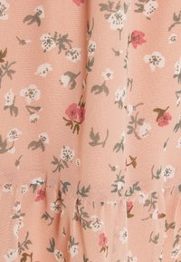Tissu pêche doux avec un motif floral de petites fleurs blanches et roses et des feuilles vertes avec de légères fronces.