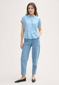 Camicia azzurra a maniche corte con stampa floreale, dal taglio morbido, abbinata a jeans azzurri a gamba affusolata e ballerine nere.