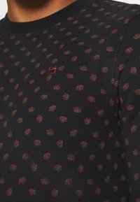 Long-sleeve black shirt with a scattered red leaf pattern and a small red logo. Made from smooth fabric with a fitted design.