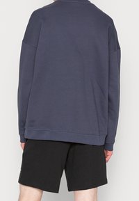 Tummansininen huppari, jossa on rento leikkaus, pitkät hihat ja ribbineulokset kauluksessa ja helman ympärillä, yhdistettynä mustiin shortseihin.