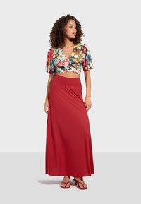 Květinový krátký top s volánkovými rukávy, spárovaný s dlouhou, jednobarevnou červenou sukní. Oblečení je vyrobeno z lehké tkaniny, což vytváří splývavý vzhled.