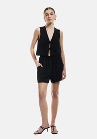 Zwarte crop top met een diepe V-hals en strik aan de voorkant, gecombineerd met zwarte shorts met koord. Geweven stof, minimalistisch ontwerp.