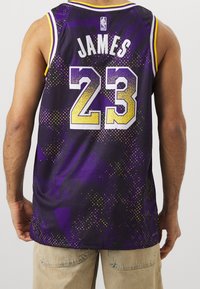 Fioletowy strój baskettowy z nazwiskiem "JAMES" i numerem "23" w białym i żółtym kolorze. Teksturowana tkanina z rozmytym wzorem oraz logo NBA.