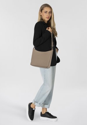 Beige Leder-Umhängetasche in eleganter, rechteckiger Form mit schwarzer Paspelierung. Kombiniert mit einem schwarzen Blazer und hellblauen, aufgerollten Jeans.