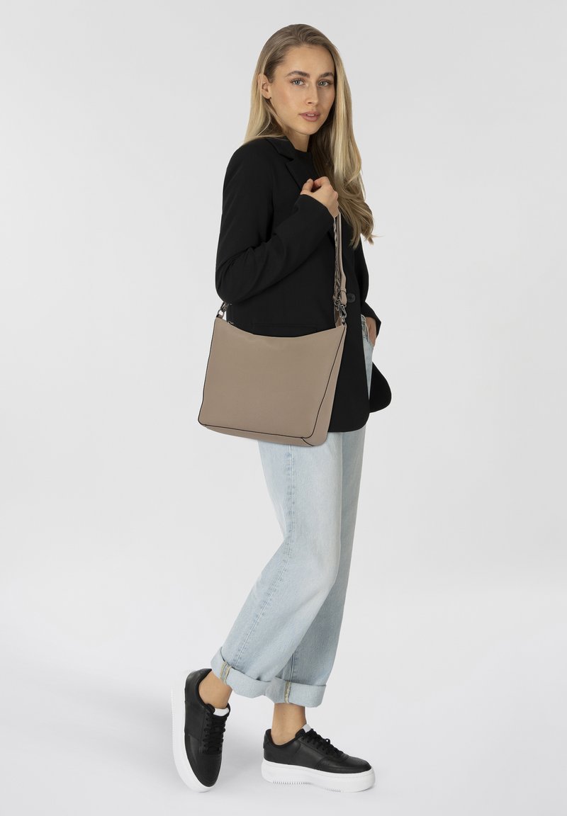 Beige Leder-Umhängetasche in eleganter, rechteckiger Form mit schwarzer Paspelierung. Kombiniert mit einem schwarzen Blazer und hellblauen, aufgerollten Jeans.