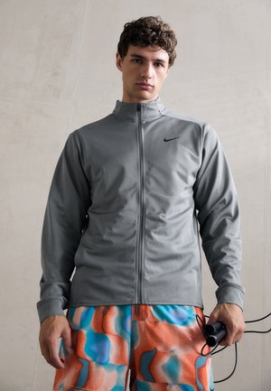 Grå zip-up jakke med ståkrave, pryder Nike-logoen på venstre bryst; bæres med shorts i flerfarvet mønster.