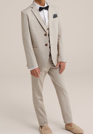 Vaaleanbeige puku yksirivisellä takilla, ruskeilla nappeilla, valkoisella paidalla ja mustalla rusetilla. Viimeistelty beigenvärisillä loafer-kengillä.