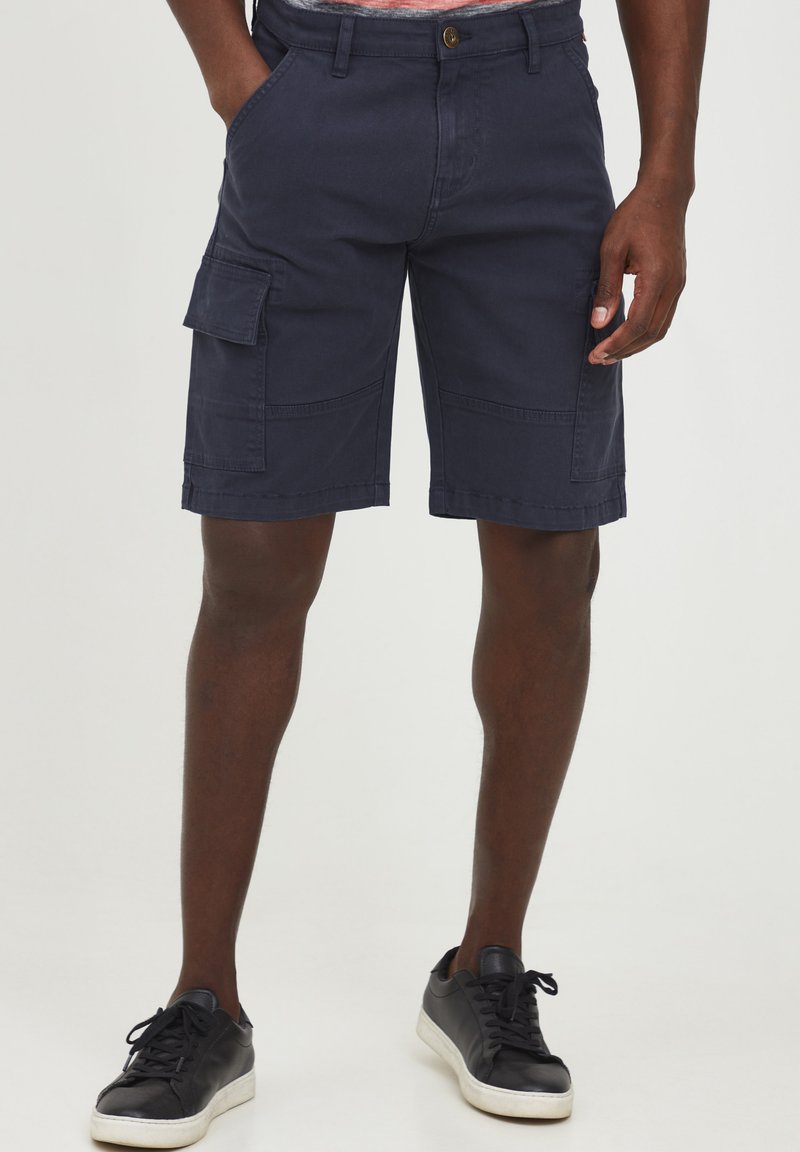Pantalones cortos de carga en algodón de color navy con bolsillos laterales, detalles de costura y cierre de botón. Combinados con zapatillas negras.