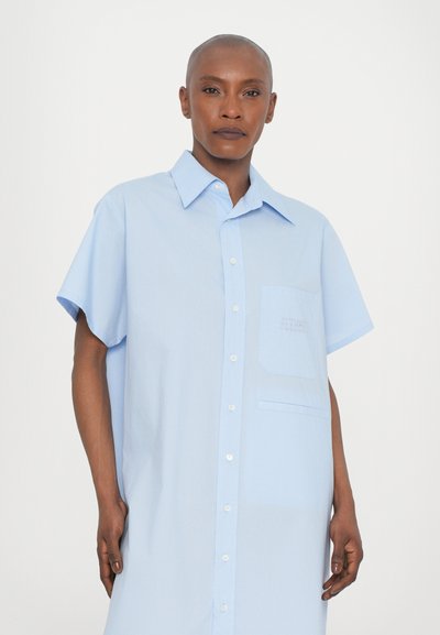 Camicia azzurra a maniche corte con colletto, bottoni sulla parte anteriore e taschino sul petto con un dettaglio texture. Tessuto dalla texture liscia.