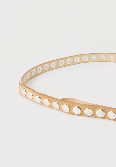 Ceinture en suède beige avec de gros clous ronds argentés régulièrement espacés sur toute sa longueur, présentée enroulée sur un fond clair.