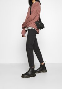 Bottes Chelsea noires avec surpiqûres jaunes, jeans noirs fuselés et un sweat-shirt oversize rose poussiéreux superposé à un haut gris.