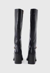 Μαύρες δερμάτινες μπότες μέχρι το γόνατο με ελαφρώς γυαλιστερό φινίρισμα, τακούνι μπλοκ, κλείσιμο με φερμουάρ και διακοσμητικές λουρίδες με χρυσές λεπτομέρειες εξαρτημάτων.