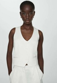 Gilet en lin blanc avec un décolleté en V profond, comportant des boutons à l'avant et des poches latérales. Le design est ajusté et de style minimaliste.