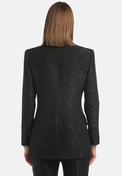 Čierny blazer s textúrovanou látkou, ktorý obsahuje jemný lesk a priliehavý strih. Výrazné detaily gombíkov na rukávoch a jediný rozvent.