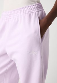 Šviesiai purpuriniai treniruokliai su elastingu juosmeniu ir šoninėmis kišenėmis, su subtiliu įspaustu 'Calvin Klein' logotipu ant kojos.