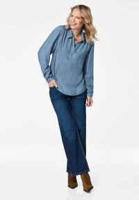 Hellblaues Button-Up-Hemd mit langen Ärmeln, kombiniert mit dunkelblauen weiten Jeans und braunen Ankle Boots. Glatter Stoff mit lässigem Schnitt.