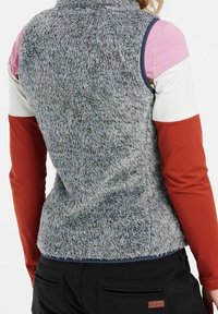 Grau, flauschige ärmellose Weste mit hohem Kragen, kombiniert mit mehrfarbigen langen Ärmeln in Rosa-, Weiß- und Rosttönen. Schwarze Hosen sind sichtbar.