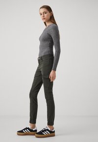 Siva rebrasta dugorukava majica u kombinaciji s tamnozelenim tapered cargo hlačama. Model nosi crne tenisice s bijelim i smeškim detaljima.