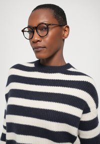 Pull rayé marine et crème avec une texture côtelée et un col rond, associé à des lunettes rondes en écaille de tortue.