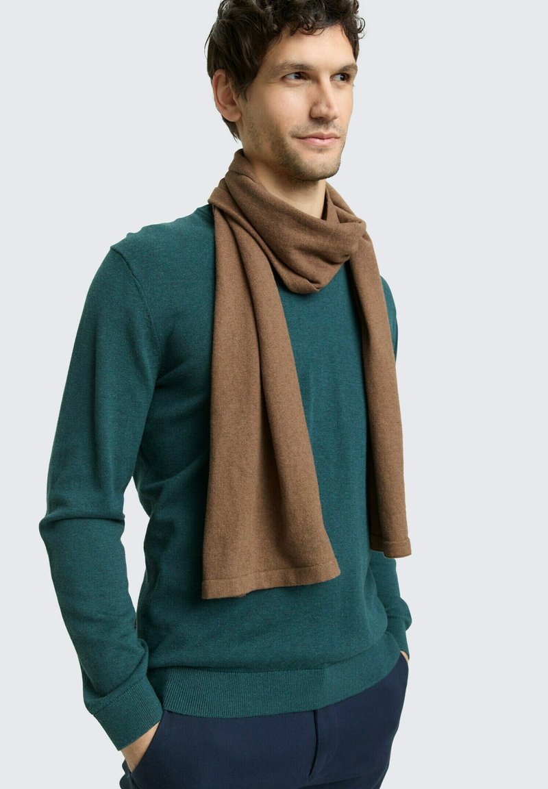 Sciarpa marrone drappeggiata intorno al collo, abbinata a un maglione verde. La sciarpa ha una consistenza morbida, mentre il maglione presenta una vestibilità classica.