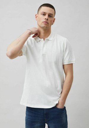 Hvid polo shirt med klassisk krave og tre knapper, lavet af glat stof. Sammen med mørkeblå jeans, minimal branding synlig.
