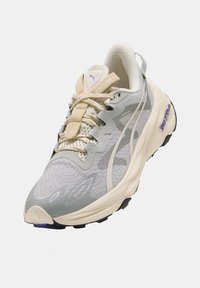 Scarpa da corsa grigia chiara con tomaia in tessuto testurizzato, lacci crema e dettagli viola. Presenta una suola imbottita e un tallone rinforzato.