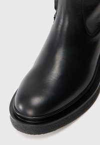 Zwarte leren enkelboot met een gladde textuur, ronde neus en een dikke rubberen zool. Verstevigde stiksels en minimale detailing.