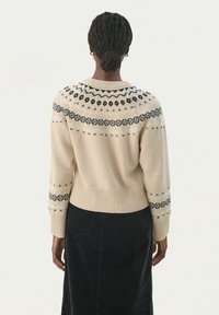 Pull beige avec un col rond et des motifs géométriques noirs sur les épaules et les manches. Tissu tricoté avec un ourlet et des poignets côtelés.