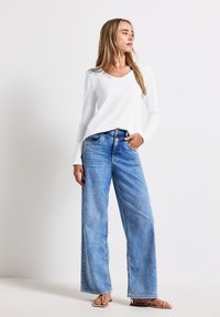 Hvid langærmet V-hals top, parret med brede lyseblå denim jeans. Blødt stof med en afslappet pasform og subtil vaskeeffekt.