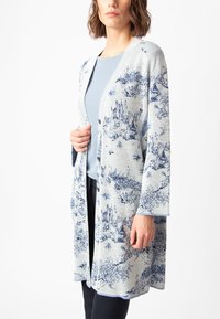 Lengvas kimono kardiganas, mėlynas ir pilkas, su peizažo spauda. Atviras priekis, ilgos rankovės, minkšta tekstūra. Dėvimas ant šviesiai mėlyno marškinėlio.
