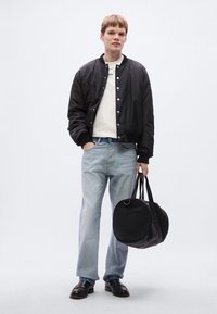 Μαύρο μπουφάν τύπου μπόμπερ με κουμπιά πατιλέτα, κρεμ φούτερ, ανοιχτό μπλε τζιν με ίσια μπατζάκια και κρατώντας μια στρογγυλή μαύρη τσάντα. Μαύρα λοφάρια ολοκληρώνουν την εμφάνιση.